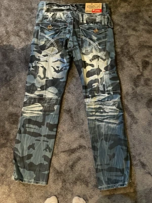 Camo jeans från Mischief - Säljer ett par camofärgade jeans från Mischief med coola detaljer som kontrastsömmar och knappar på bakfickorna. Jeansen har en unik tvätt och patch på linningen. Perfekta för dig som vill sticka ut med din stil.
