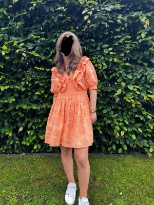 Orange klänning med volanger - Söt orange kortklänning med broderade detaljer och volanger framtill. Klänningen har v-ringning och puffiga korta ärmar. Storlek 38 men passar även 36