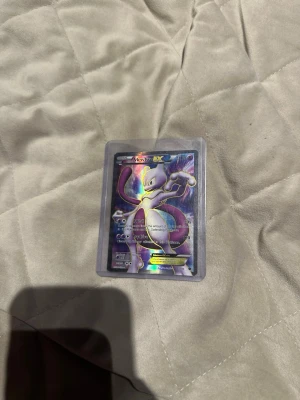 Pokémonkort Mewtwo EX - Säljer ett Pokémonkort med Mewtwo EX-motiv. Kortet har en holografisk yta och ligger i ett genomskinligt plastfodral. Perfekt för samlare eller Pokémonfans som vill utöka sin samling.