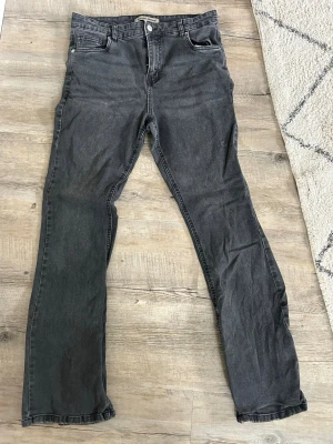 Mörk grå raka jeans - Säljer ett par mörkgrå  jeans med klassiska raka ben. Jeansen har blixtlås och knappstängning och är tillverkade i denim. Stretchiga sköna jeans kommer troligen från Lindex, står Denim Rebel. 