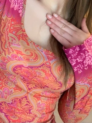 Mönstrad långärmad topp i rosa och orange - Säljer en färgstark långärmad topp med paisley- och blommönster i rosa, orange och gula toner. Toppen har en djupare rundringning och är figurnära i modellen. Materialet känns mjukt och stretchigt, perfekt för dig som gillar statement-plagg.