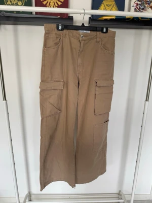 Beiga cargobyxor från Bershka - Säljer ett par beiga cargobyxor från Bershka med  raka ben och flera stora fickor på sidorna. Byxorna är i storlek 42