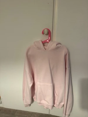 Ljusrosa hoodie från 157 - Mysig ljusrosa hoodie från 157 med klassisk huva och stor magficka. Tillverkad i mjukt material som känns skönt mot huden. Perfekt för dig som gillar en enkel och clean stil. Ribbade muddar vid ärmslut och nederkant för extra komfort.