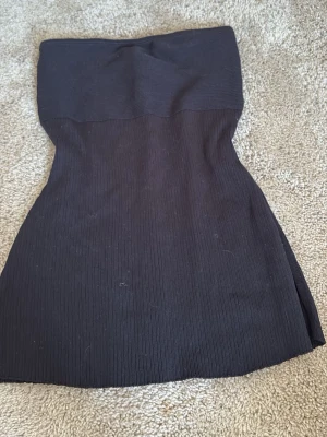 Svart ribbad tubtopp - Säljer en svart ribbad tubtopp med slits på sidan. Toppen har en kroppsnära passform och är gjord i ett stretchigt material som formar sig efter kroppen. Perfekt för dig som gillar minimalistisk stil.