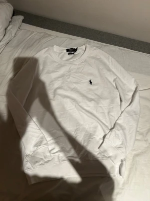 Vit sweatshirt från Ralph Lauren - Klassisk vit sweatshirt från Ralph Lauren med rund halsringning och den ikoniska mörkblå polospelaren broderad på bröstet. Tröjan har långa ärmar och ribbade muddar vid ärmslut och nederkant. Perfekt basplagg i mjukt bomullsmaterial. Ganska skön tröja storlek L men passar perfekt för även  M då jag bär på storlek M helt ny bara testat 