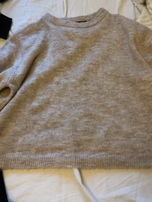 Beige stickad tröja i ullmix - Mysig beige stickad tröja med rund hals och långa ärmar. Tröjan har en avslappnad passform och ribbade muddar vid ärmslut och nederkant. Perfekt för lager på lager och enkel att matcha till olika outfits.
