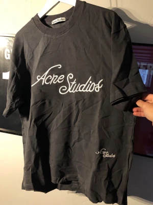 Svart Acne Studios t-shirt - Snygg svart t-shirt från Acne Studios med vit broderad logga framtill och mindre logga nedtill. Klassisk rund halsringning och korta ärmar. Perfekt basplagg med stilren design och skön passform.