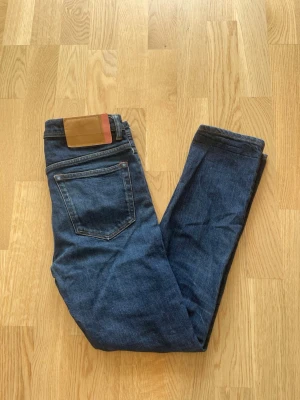 Mörkblå jeans från Acne Studios W30 L34 - Jag säljer dom här riktigt snygga jeansen från Acne Studios i storlek W30 L34. Dom är i fint skick utan skador och defekter. Modellen heter River Indigo. Tveka inte att höra av er!                 Mått: Längd=95cm. Midja=40cm