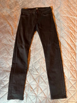 Svarta jeans från Lee - Säljer ett par svarta jeans från Lee med klassisk femficksdesign och snygg passform. Jeansen har Lee-logga på bakfickan och är tillverkade i stretchigt denimtyg för extra komfort. Perfekta för en stilren och enkel look.