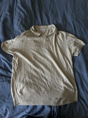 Beige polotopp från Zara XL - Klassisk beige polotopp från Zara i storlek XL. Toppen har korta ärmar, krage och knappar vid halsen. Tillverkad i mjukt material med ribbade muddar nedtill och vid ärmsluten. Perfekt för en clean och stilren look.