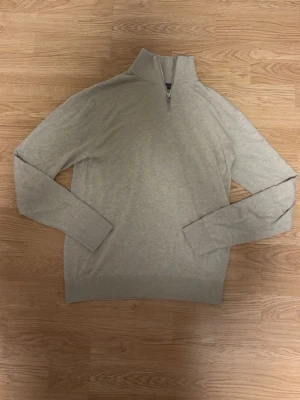 Beige stickad tröja med halv dragkedja - Säljer en helt ny snygg beige stickad tröja med halv dragkedja i halsen. Tröjan har långa ärmar, ribbade muddar och nederkant. Perfekt för lager på lager och enkel att matcha med olika outfits.