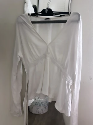Vit omlottopp från Gina Tricot - Säljer en vit omlottopp från Gina Tricot i mjukt material. Toppen har långa ärmar, v-ringning och knytband i midjan för en snygg passform. Perfekt att styla med jeans eller kjol för en trendig look. Jag säljer denna tröja lite dyrare eftersom den inte säljs på Ginatricot längre vad jag minns och inte haft på mig den så mycket alls så den är ganska ny🤍