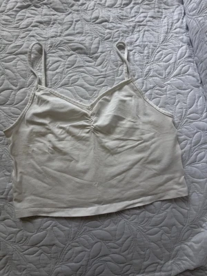 Vit croppad linnetopp från H&M Divided - Säljer en enkel och stilren vit croppad linnetopp från H&M Divided. Toppen har tunna axelband, lätt rynkning vid bysten och är tillverkad i mjuk bomull. Perfekt till sommaren och enkel att matcha med allt.