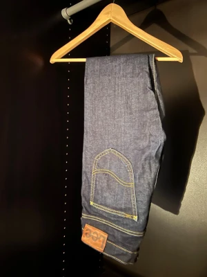 Mörkblå  jeans från Lee - Säljer ett par mörkblå skinny jeans från Lee med klassiska gula sömmar och femficksmodell. Jeansen har en rak passform och Lee-lapp bak i midjan. Materialet är denim i bomull med lite stretch för extra komfort