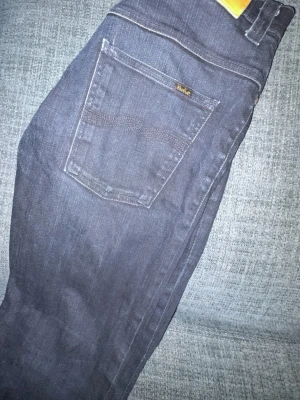 Mörkblå jeans från Nudie Jeans - Snygga mörkblå jeans från Nudie Jeans med klassisk femficksmodell och slim fit. Jeansen har kontrastsömmar och en liten Nudie-logga på bakfickan. Tillverkade i mjukt denimtyg som sitter skönt hela dagen. Storlek 30/31