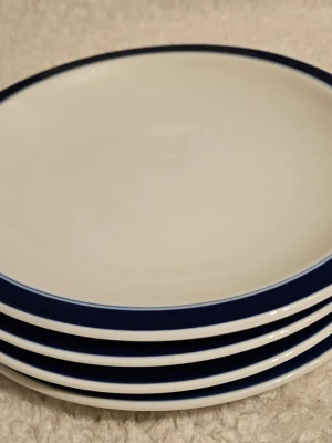 Fyra Rörstrand VDN P555 tallrikar - Säljer fyra runda tallrikar i vitt porslin med en stilren blå kant runt hela tallriken. Perfekta för att duka upp till middag eller fika. Klassisk design som passar de flesta kök och matbord.
