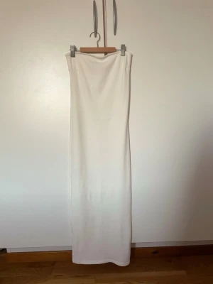 Vit långkjol i ribbad bomull - Säljer en enkel och stilren vit långkjol i ribbad bomull. Kjolen har en rak passform och är stretchig, vilket gör den bekväm och lätt att styla 