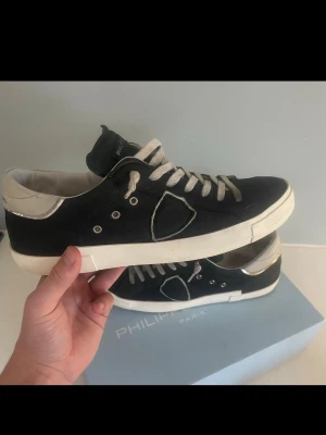Philippe Model  sneakers - Blå sneakers från Philippe Model med vita detaljer och vita skosnören. Skorna har en vit sula, silverfärgade detaljer vid hälen och en ikonisk sköld på sidan. Tillverkade i läder och textil för en clean och stilren look.