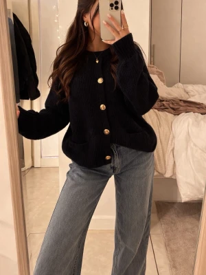 Stickad tröja  med guldknappar - Säljer en svart, ribbstickad kofta från Gina Tricot med stora guldknappar framtill och två fickor. Koftan har rund halsringning och långa ärmar, perfekt att slänga över en t-shirt eller topp.