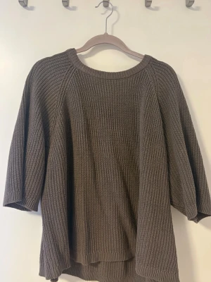 Brun stickad tröja med trekvartsärm - Mysig brun stickad tröja med bred halsringning och trekvartsärmar. Tröjan har en avslappnad passform och är ribbstickad i ett mjukt material. 