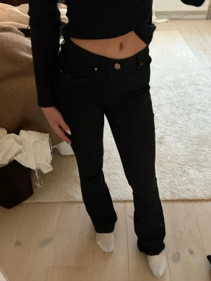 Svarta raka jeans med låg midja - Säljer ett par svarta jeans med låg midja och bootcut ben. Klassisk femficksmodell med knapp och dragkedja framtill. Jeansen har en enkel och stilren look som passar till det mesta. Perfekta för dig som gillar en clean och tidlös stil.