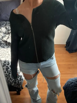 Mörkgrön cardigan jacka från Vila - Snygg mörkgrön cardigan jacka från Vila i storlek L. Jackan har ett diskret mönster, rund halsringning och dragkedja framtill. Materialet är mjukt och känns lite stickat, perfekt för dig som gillar stilrena och bekväma plagg. Det står storlek L men den passar M-S