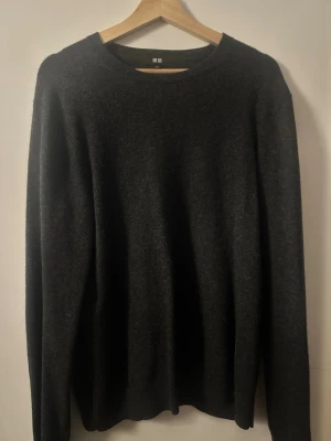 Cashmere mörkgrå stickad tröja från Uniqlo - En enkel och stilren mörkgrå stickad tröja från Uniqlo. Tröjan har rund halsringning och långa ärmar. Perfekt basplagg i garderoben och passar till det mesta. Materialet känns mjukt och bekvämt.