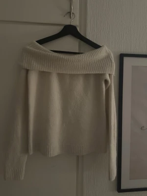 Off shoulder stickad tröja Gina Tricot - Krämvit stickad tröja från Gina Tricot med bred off shoulder-krage och långa ärmar. Tröjan har ribbstickade detaljer vid krage, ärmslut och nederkant. Perfekt för dig som gillar en avslappnad men trendig stil.