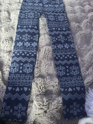 Mörkblå leggings med snöflingor - Supersnygga mörkblå leggings med ljusblått vintermönster av snöflingor, hjärtan och zigzag-detaljer. Stretchigt material och bred midjeresår för skön passform. Perfekta för dig som vill ha något mysigt och stilrent till vintern.