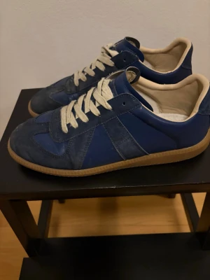 Marinblå sneakers med mockadetaljer - Snygga marinblå sneakers med beige sula och vita snören. Skorna har en klassisk låg siluett och är tillverkade i en mix av mocka och slätt läder. Insidan är fodrad i beige textil för extra komfort. Perfekta för en clean och stilren look.