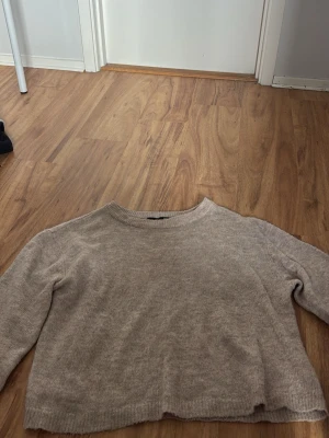 Beige stickad tröja från 157 - En enkel och stilren beige stickad tröja från 157 med rund halsringning och långa ärmar. Tröjan har en mjuk och avslappnad passform, perfekt för lager på lager. Ribbstickade muddar vid hals, ärmslut och nederkant ger en klassisk look. Lite smink vid kragen men går att tvätta bort 