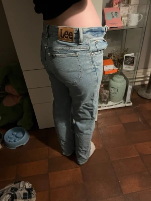 Ljusblå raka jeans från Lee - Säljer ett par ljusblå jeans från Lee med rak passform och klassisk femficksdesign. Jeansen har hög midja och Lee-logga på bakfickan. Tillverkade i denim med en avslappnad look, perfekta för en casual stil.