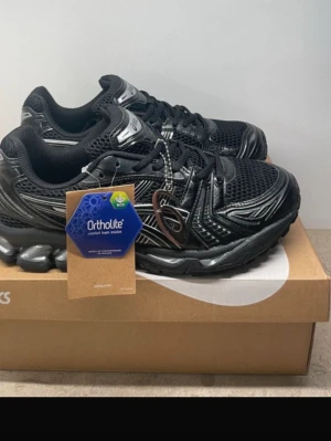  Asics  - Snygga svarta sneakers från Asics med coola meshpaneler och detaljer i syntet. Skorna har Ortholite-innersula för extra komfort och en chunky sula som ger streetkänsla. Perfekta för dig som gillar sportig stil och vill ha något som sticker ut.