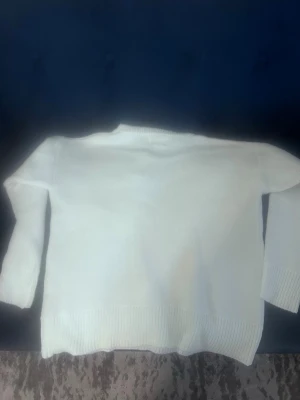 Vit stickad tröja från Ami Paris - Säljer en stilren vit stickad tröja från Ami Paris. Tröjan har rund halsringning, långa ärmar och ribbade muddar vid ärmslut och nederkant. Perfekt för dig som gillar minimalistisk och klassisk stil.