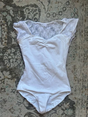 Vit dans dräkt  - En vit balett body/dräkt med spets i ryggen. Kan användas till fest eller till balett/dans lektioner. Fint skick! Bortklippt lapp men passar xs-s
