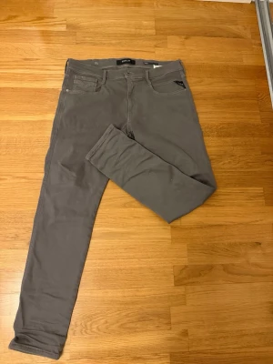 Grå slim fit jeans från Replay - Snygga grå jeans från Replay, modell Anbass med slim fit passform. Klassisk femficksdesign och dragkedjegylf. Perfekta för dig som gillar en stilren och modern look.