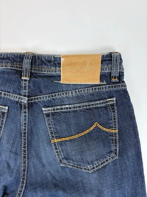 Blå jeans från Jacob Cohen - Snygga blå jeans från Jacob Cohen med klassisk femficksmodell och kontrastsömmar. Jeansen har en rak passform och detaljerad bakficka med gul söm samt en beige patch med logga i midjan. Tillverkade i mjukt denimtyg som ger en avslappnad look.