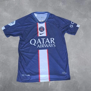 PSG fotbollströja  - Säljer en officiell Paris Saint-Germain fotbollströja med Mbappé 7 på ryggen. Tröjan är blå med vita och röda detaljer, har korta ärmar och är tillverkad i lätt, ventilerande material. PSG-logga och Qatar Airways-tryck på bröstet, Nike swoosh och sponsortryck på ärmarna. Skulle säga att den passar M/L.
