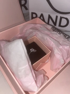 Silverring med sten från Pandora - Säljer en elegant silverring från Pandora med en gnistrande klar sten i mitten. Ringen har en klassisk och stilren design, perfekt för dig som gillar tidlösa smycken. Levereras i originalask med rosa och svart inredning.