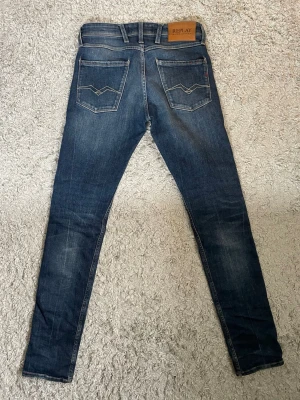 Mörkblå jeans från Replay W28 L34 - Snygga mörkblå jeans från Replay med klassisk femficksdesign och kontrastsömmar. Priset är inte spikat, Skulle säga att de passar någon som är runt 170-175 lång, Jeansen har en läderpatch med logga bak i midjan och coola detaljer på bakfickorna. Tillverkade i stretchig denim för skön passform.