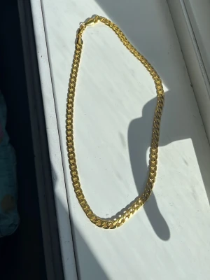Guldfärgat kedjehalsband - Snyggt halsband i guldfärg med platt, bred kedja och klassiskt karbinlås. Halsbandet har en stilren och modern design som passar perfekt till olika outfits. 