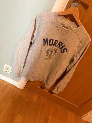 Grå sweatshirt från Morris - Grå sweatshirt från Morris med rund halsringning och tryckt logga i mörkblått framtill.