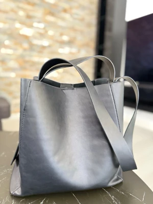 Stilren svart shoppingväska i läder - Snygg och minimalistisk shoppingväska i svart läder med både korta och långa handtag. Enda defekten i form av en uppklipt lapp inuti i väskan, inget som man märker av. Rymmer allt du behöver till skolan, jobbet eller stan.