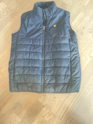 Mörkblå dunväst från Lyle & Scott - Snygg mörkblå dunväst från Lyle & Scott med gul logga på bröstet. Säljs då den inte används. Priset kan diskuteras vid snabb affär. Kontakta mig vid frågor eller bilder! 