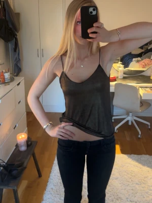 Svart glittrig linnetopp - Snygg svart glittrig linnetopp med tunna axelband och v-ringning. Toppen är croppad och har en lätt glansig finish som ger en trendig look. Perfekt att styla med jeans eller kjol för en cool outfit.