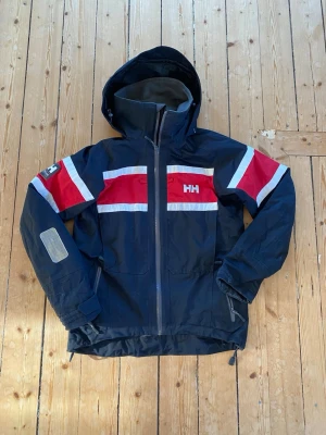 Helly Hansen jacka - Snygg Helly Hansen jacka i marinblå med vit, röda detaljer. Namn på insidan är överstruket. Storlek xs. Köptes till min bror. Nypris cirka 4000kr