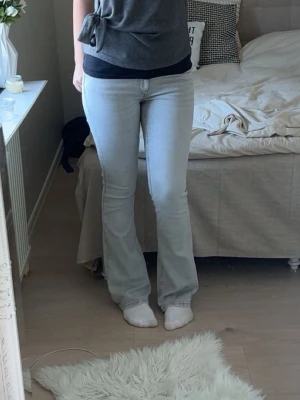 Grå TALL bootcut jeans - Säljer ett par grå bootcut jeans med klassisk femficksdesign med låg midja. Jeansen har en snygg utsvängd passform nedtill och är perfekta för en avslappnad men trendig look. Passar dig som gillar retrovibbar och ljusa tvättar. 