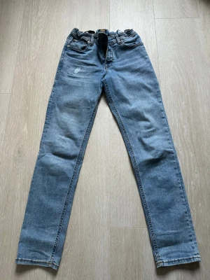 Ljusblå raka jeans från Jack & Jones - Säljer ett par ljusblå jeans från Jack & Jones med klassisk femficksdesign och raka ben. Jeansen har en liten sliten detalj framtill och patch med logga bak i midjan. Perfekta för en avslappnad och trendig look.