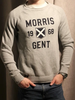 Tunn Grå tröja Morris - Snygg grå tröja från Morris med tryck 'Morris Gent 1968' och ett sköldmärke på bröstet. Tröjan har rund hals, ribbade muddar och är tillverkad i mjukt stickat material. Perfekt för en avslappnad och stilren look.