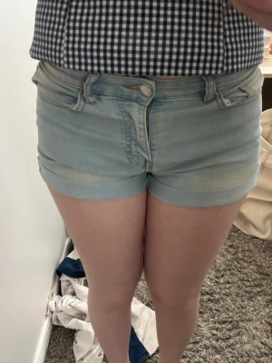 Ljusblå jeansshorts med uppvik - Snygga ljusblå jeansshorts med uppvikta benslut och klassisk femficksdesign. Perfekta för varma dagar och enkla att matcha med olika toppar. Stängs med dragkedja och knapp framtill.